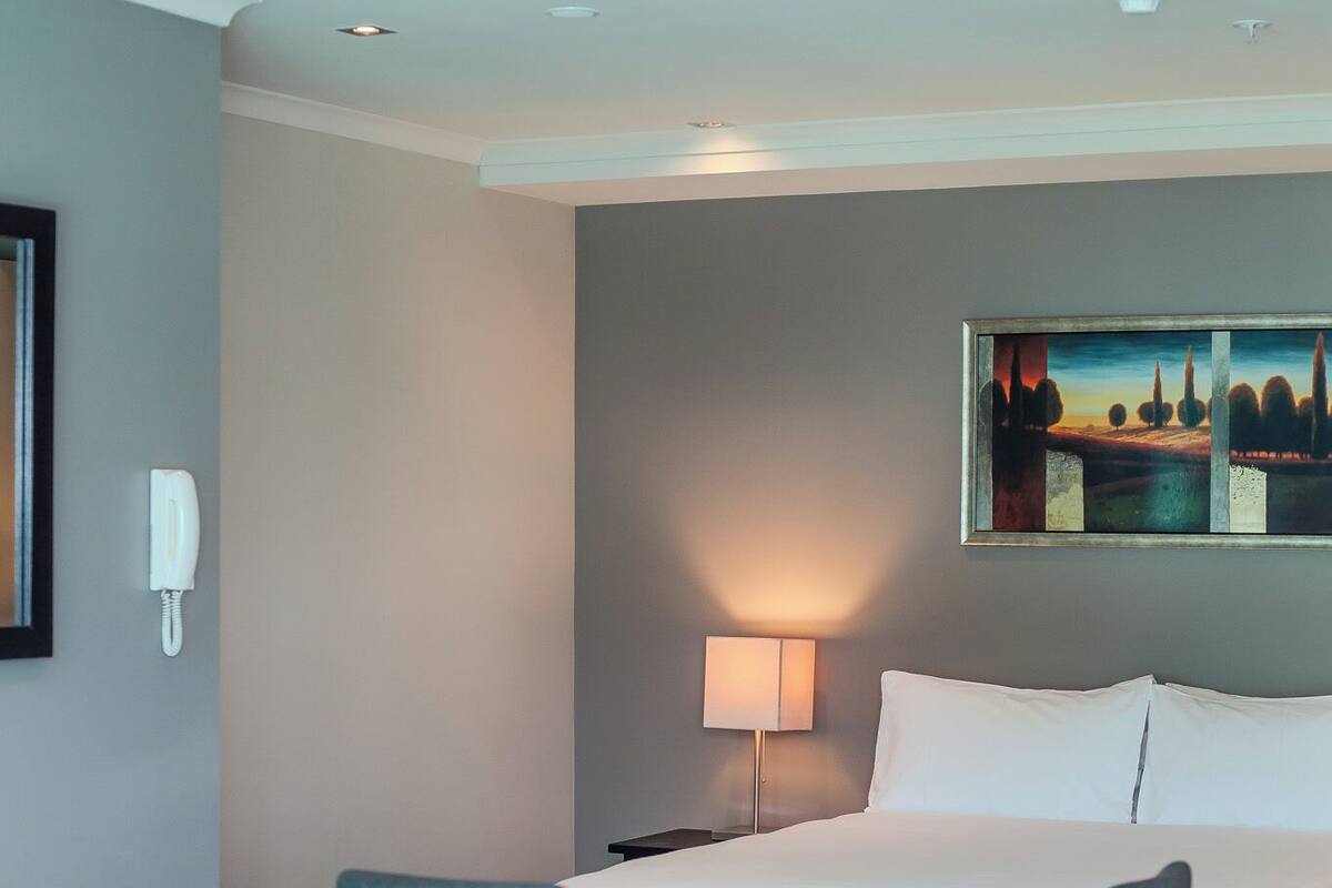A hotel room with a bed, a desk with a chair, a lamp, and a painting on the wall.