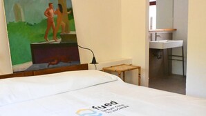 Camera d'albergo con un letto, un quadro, un tavolino e un bagno visibile attraverso una porta aperta.