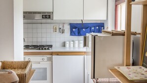 Una cucina compatta con mobili bianchi, piano cottura a gas, forno integrato e frigorifero.