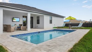 Ett modernt hus med en swimmingpool, utomhusmöbler och en TV som är monterad på väggen.