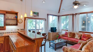 Uma sala de estar ampla com uma mesa de jantar de madeira, um conjunto de sofá e uma televisão sobre um móvel.
