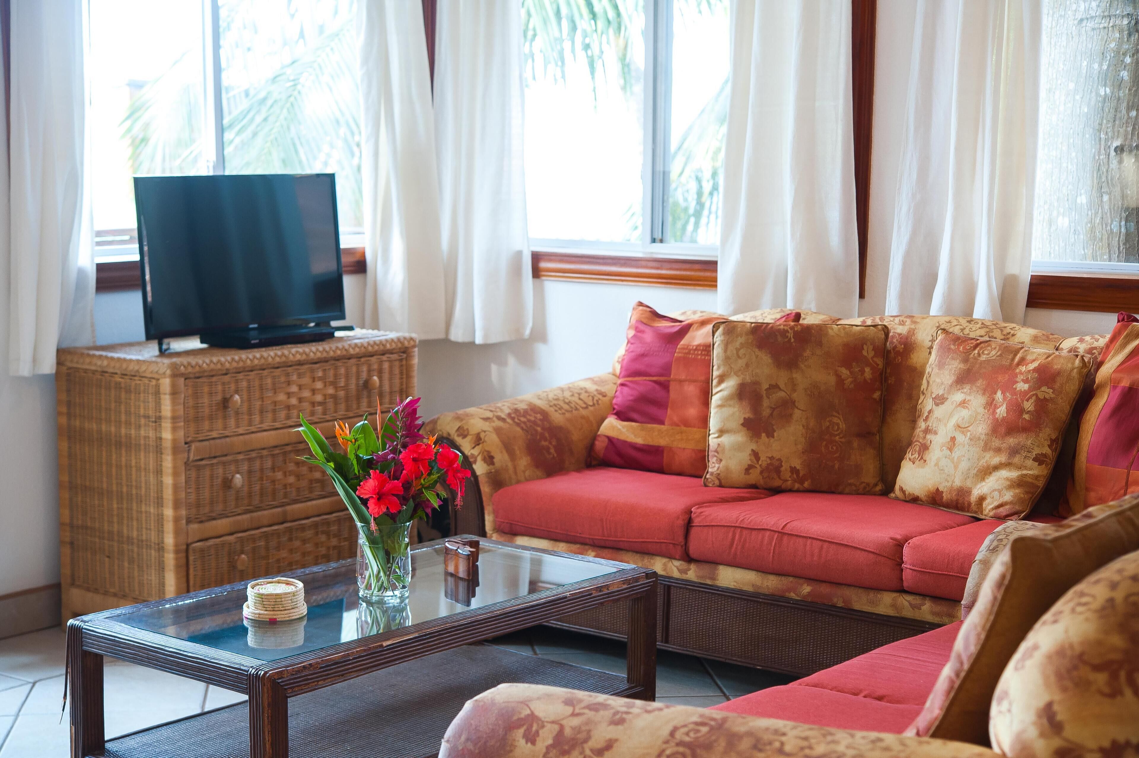 Ein Wohnzimmer mit einer Couch, einem Fernseher auf einem Schrank, einem Couchtisch und einem Korbschrank.