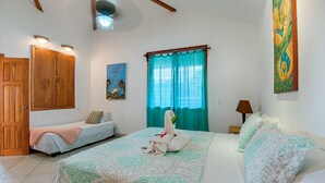 Quarto de hotel com cama, um banquinho, um quadro e janela com cortinas.