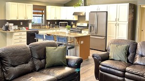Ein großzügiger Wohnbereich mit Ledersofas, eine Küche mit weißen Schränken, einem Kühlschrank und ein Essbereich mit Tisch und Stühlen.