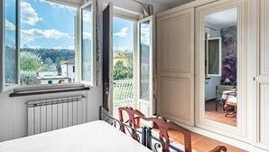 Een slaapkamer met een groot raam, een radiator, een bed en uitzicht op een balkon.