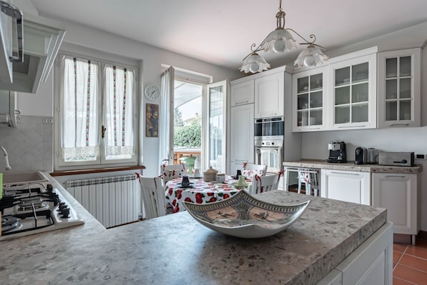 A kitchen with white cabinets, a gas stove, a dining table with a patterned tablecloth, and a decorative bowl on the counter.