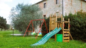 A rustic stone house with a wooden play structure including a slide and swings.