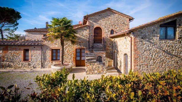A stone building with a central staircase, a palm tree, and a gravel courtyard.