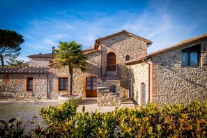 Un edificio in pietra con una scalinata centrale, una palma e un cortile sterrato.