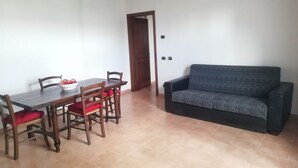 A dining area with a wooden table and chairs, a sofa, and a door leading to another room.
