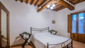 A bedroom with a wooden ceiling, a metal bed frame, a bedside table, and a window with curtains.