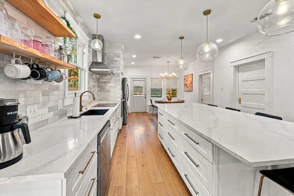 Cocina moderna con armarios blancos, una isla grande e iluminación colgante.