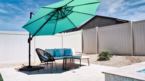 A patio with a white fence, a turquoise umbrella, a white sofa with blue cushions, and a small pool. - Modern Desert Oasis (Coachella)