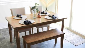 A wooden dining table with a bench, set with folded napkins and a vase of pampas grass. - Modern Desert Oasis (Coachella)