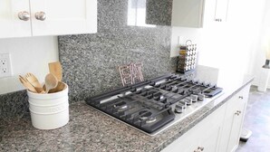 A kitchen with a granite countertop, a gas stove, and a white cabinet with a handle. - Modern Desert Oasis (Coachella)