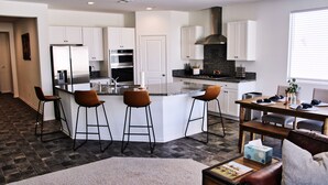 A modern kitchen with white cabinets, a stainless steel refrigerator, and a central island with bar stools. - Modern Desert Oasis (Coachella)