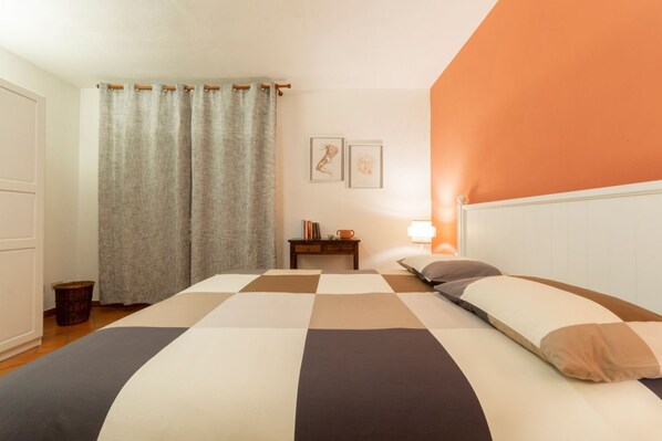 A bedroom with a checkered bedspread, a bedside table with a lamp, and a wall with two framed pictures.