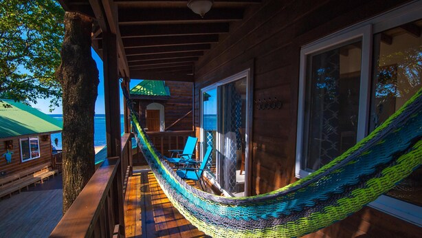 A wooden deck with a hammock, wooden benches, and a view of the ocean.