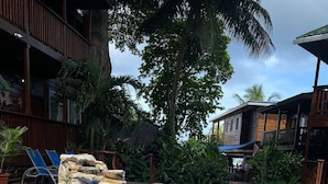 A swimming pool with a waterfall feature, surrounded by wooden deck and tropical plants.