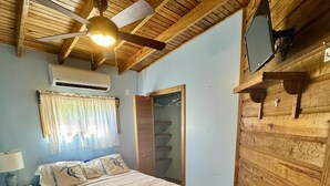A bedroom with a bed, a nightstand, a ceiling fan, an air conditioning unit, and a wooden wardrobe.