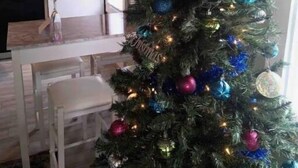 A Christmas tree decorated with ornaments and lights in a room with a neon sign reading "love" and a kitchen area in the background. - Love Shack Private Hot tub  steps to Jet/Town (Port Clinton)