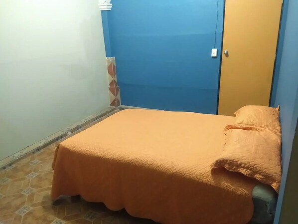 Una habitación pequeña con una cama individual, una pared azul y una puerta.