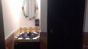 A bathroom with a tiled sink, a mirror with a floral frame, and a black door.