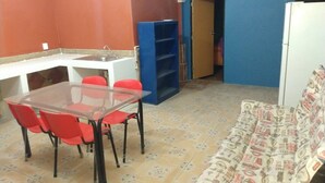 A compact living space with a dining table, red chairs, a sofa, a small kitchen area, and a blue wall.