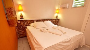 Una cama bien tendida con sábanas y toallas blancas, dos lámparas de noche, un cabecero con diseño similar a la madera y un equipo de aire acondicionado en la pared.