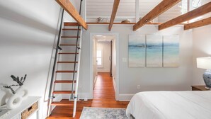 Un dormitorio con una escalera de madera, una cama, una mesita de noche y un cuadro en la pared.
