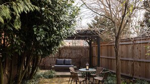 Un patio con una mesa redonda y sillas, una cerca de madera y un banco de madera con cojines.