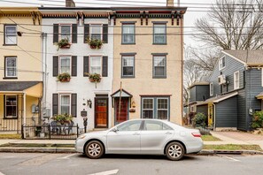 A silver car parked on a residential street with multi-story houses, including a house with a front porch and potted plants. - 'Brooke House' In The Heart of Downtown w/ Patio! (Lambertville)