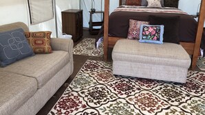 A tented accommodation with a bed, a sofa, an ottoman, and a patterned rug. - Wildlife, Nature, Glamp 1 (Cave Junction)