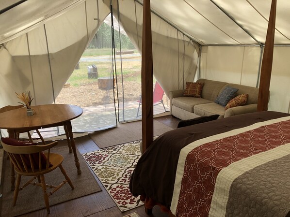 A tented accommodation with a bed, a sofa, a table, and a chair.