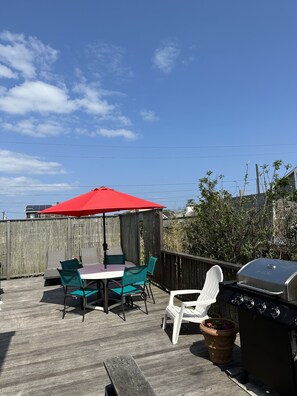 A wooden deck with a table and chairs under a red umbrella, a barbecue grill, and a wooden fence in the background. - Large Beach House Steps From Town and Ocean (Ocean Beach)