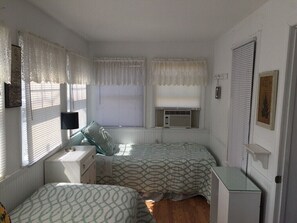 A bedroom with two beds, white walls, lace curtains, and a small bedside table with a lamp. - Large Beach House Steps From Town and Ocean (Ocean Beach)