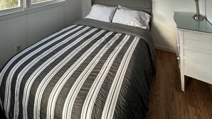 Une chambre à coucher avec un lit, une fenêtre avec des rideaux, une table de chevet avec une lampe et un tableau accroché au mur.
