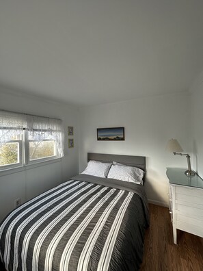 A bedroom with a bed, a window with curtains, a bedside table with a lamp, and a painting on the wall.