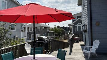 Une terrasse avec une table ronde, des chaises et un parasol rouge.