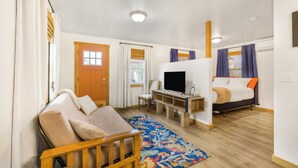 Ett kompakt hotellrum med en soffa, en säng, en TV och ett litet skrivbord.