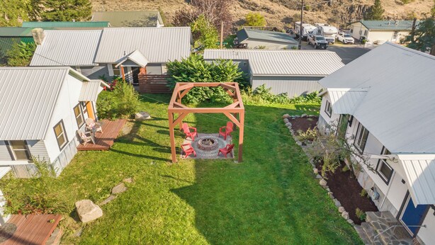 A residential area with multiple houses, a central fire pit surrounded by red chairs, and a well-maintained lawn. - Salmon River Cabin #204 (Riggins)