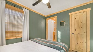 A bedroom with a bed, a ceiling fan, a wooden door, and a window with blinds. - Salmon River Cabin #204 (Riggins)