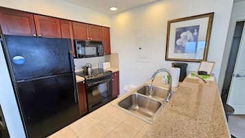 A modern kitchen with a black refrigerator, stainless steel sink, and granite countertop.
