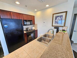 A modern kitchen with a black refrigerator, stainless steel sink, and granite countertop.