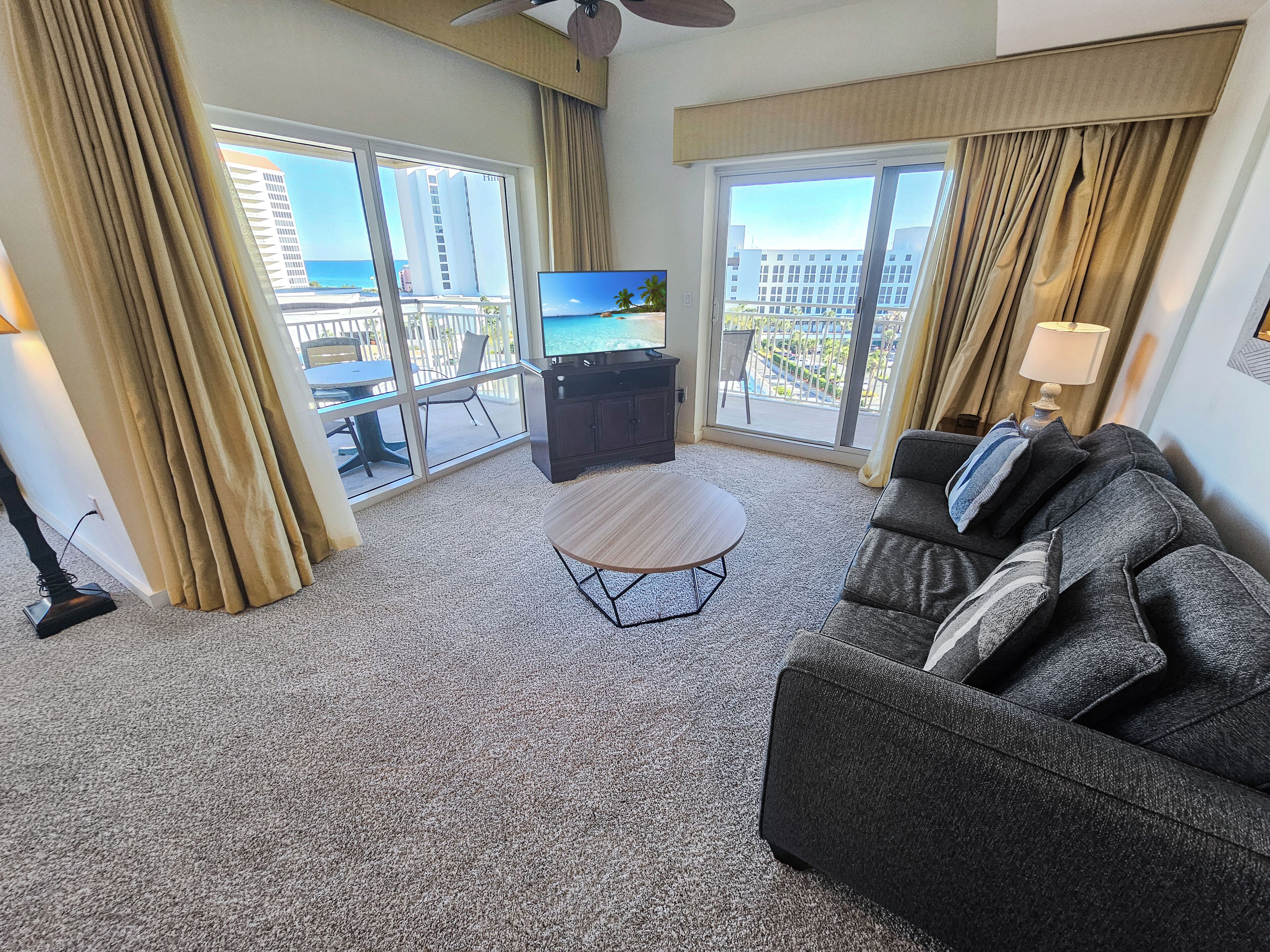 A hotel room with a balcony, a TV, a sofa, and a small table.