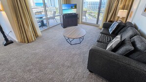 Habitación de hotel con balcón, televisor, sofá y una mesita.