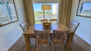 Un comedor con una mesa y sillas de madera, un cuenco grande tejido y vistas a la ciudad a través de amplios ventanales.