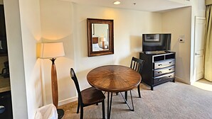 A hotel room with a round wooden table, two chairs, a TV, a lamp, and a mirror on the wall. - Luau 6533 South Facing Gulf Views! |Wifi | Tram Included (Miramar Beach)