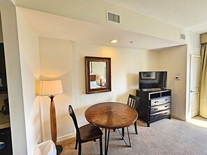 A hotel room with a round wooden table, two chairs, a TV, a lamp, and a mirror on the wall.