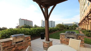 An outdoor patio with stone-built barbecue grills, a round table, and wicker chairs. - Luau 6533 South Facing Gulf Views! |Wifi | Tram Included (Miramar Beach)